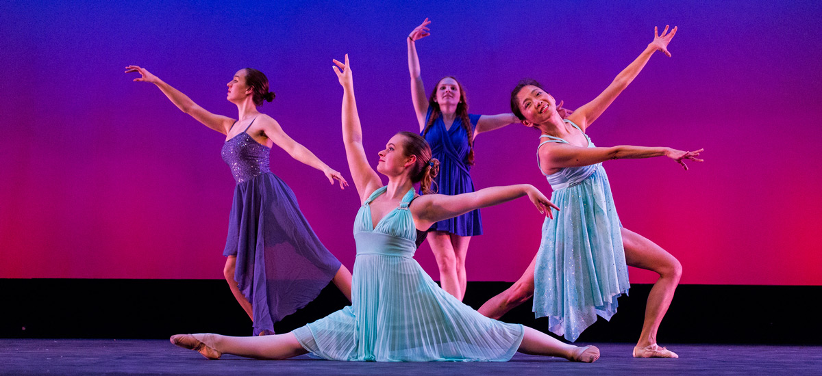 Four women in blue dresses dancing in front of gradient background