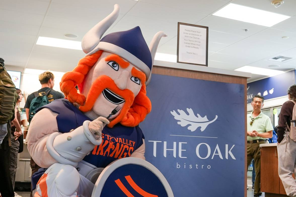 vik the viking mascot holding a fork, posing in front of the oak bistro logo