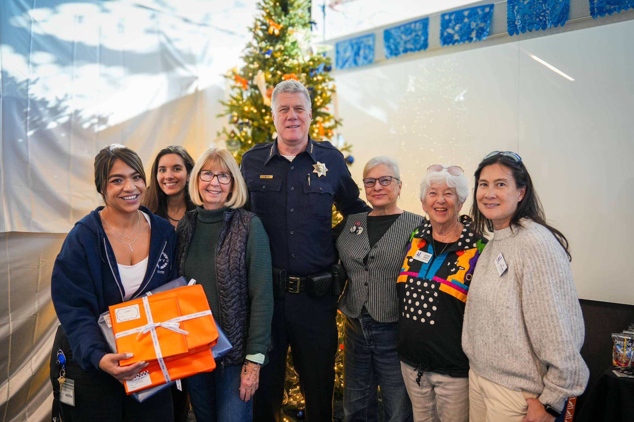 west valley college staff pictured in front of a christmas tree. one staff is holding orange wrapped presents