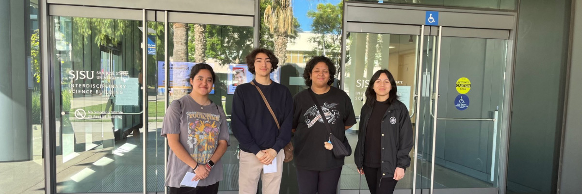 A group of four people standing in front of glass doors.