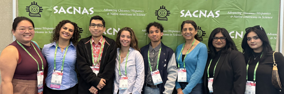 A group of people standing in front of a green banner that says SACNAS.