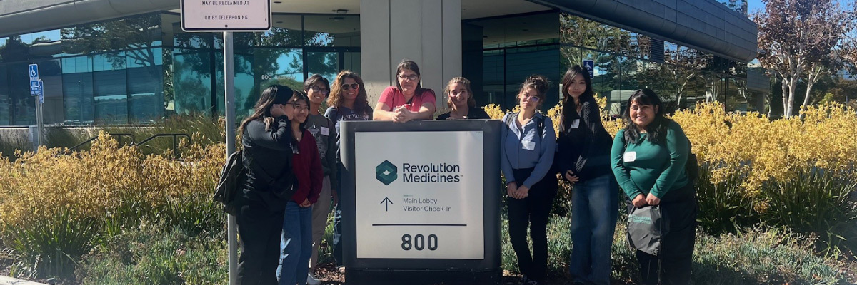 A group of people standing around a sign that says Revolution Medicines.