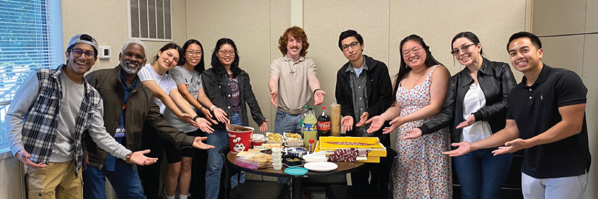 A group photo of people standing around a table full of food.