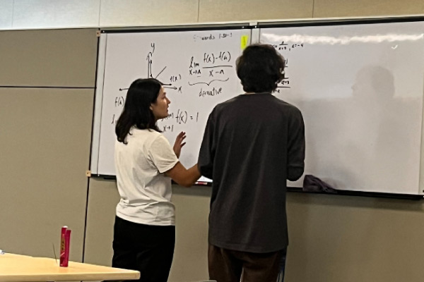 Two people standing in front of a white board.