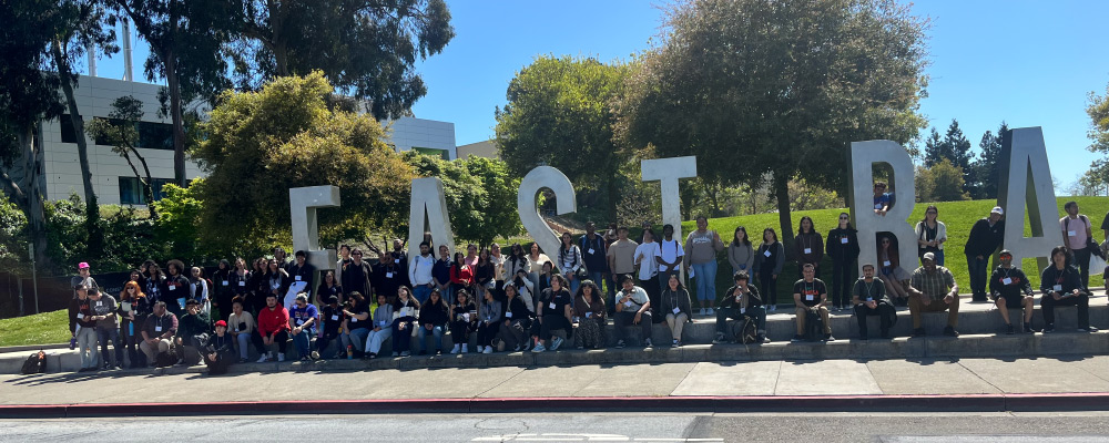 A large group of people posing in front of tall letters spelling out "East Bay"