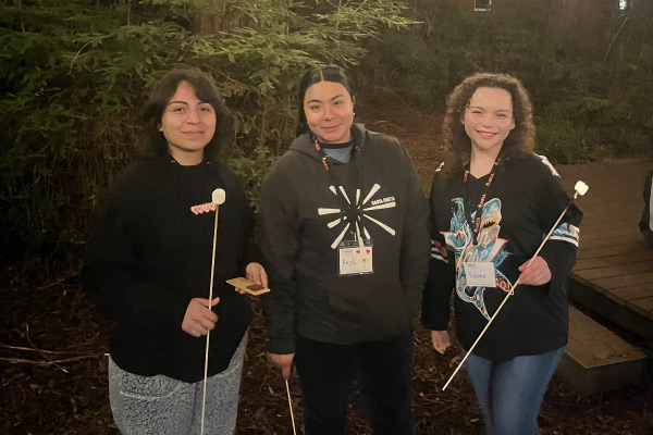 Three people holding sticks with marshmellows.