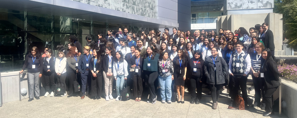 A large group of people posing for a picture outside of a gray building.